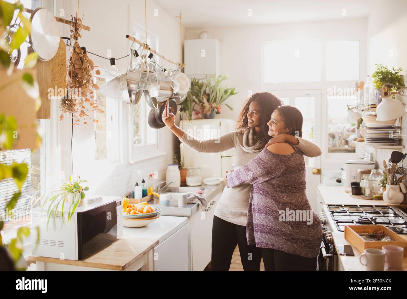 Feliz madre e hija tomando selfie en la cocina soleada Foto de stock