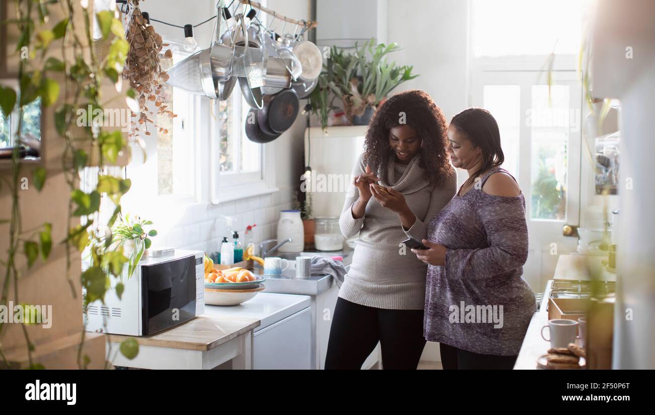 Madre e hija usando teléfonos inteligentes en la cocina Foto de stock