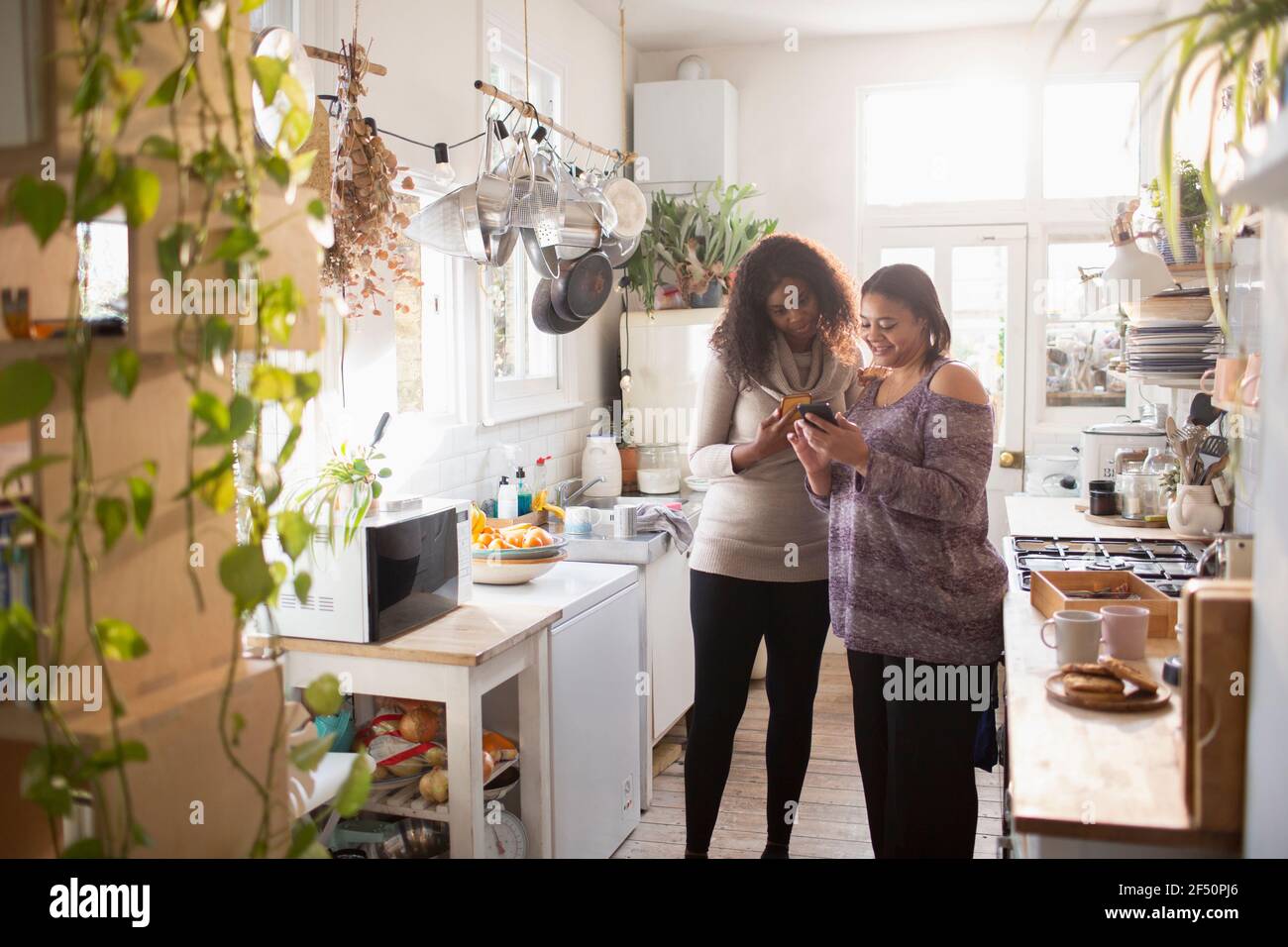 Madre e hija utilizando el teléfono inteligente en la cocina Foto de stock