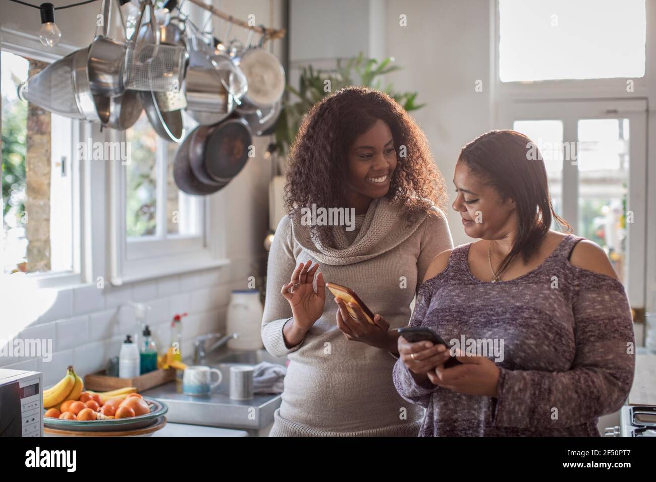 Madre e hija usando teléfonos inteligentes en la cocina Foto de stock