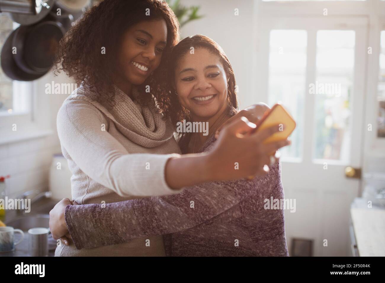 Feliz madre e hija abrazando y tomando selfie en la cocina Foto de stock