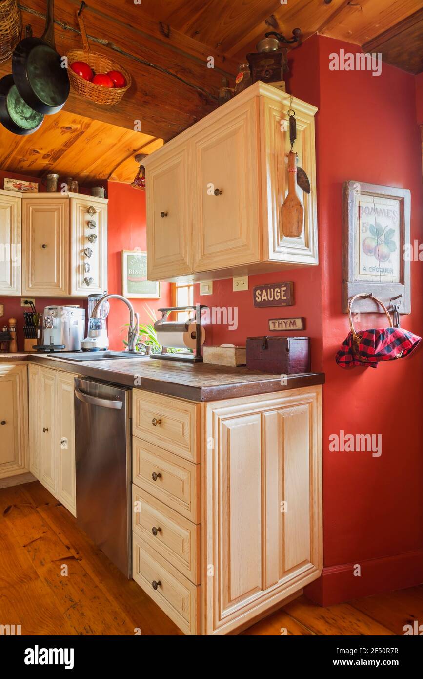 Armarios de madera de roble pintado de blanco y encimeras de cerámica con  tonos tierra en la cocina con tablas de madera de pino, paredes pintadas de  color rojo dentro de la