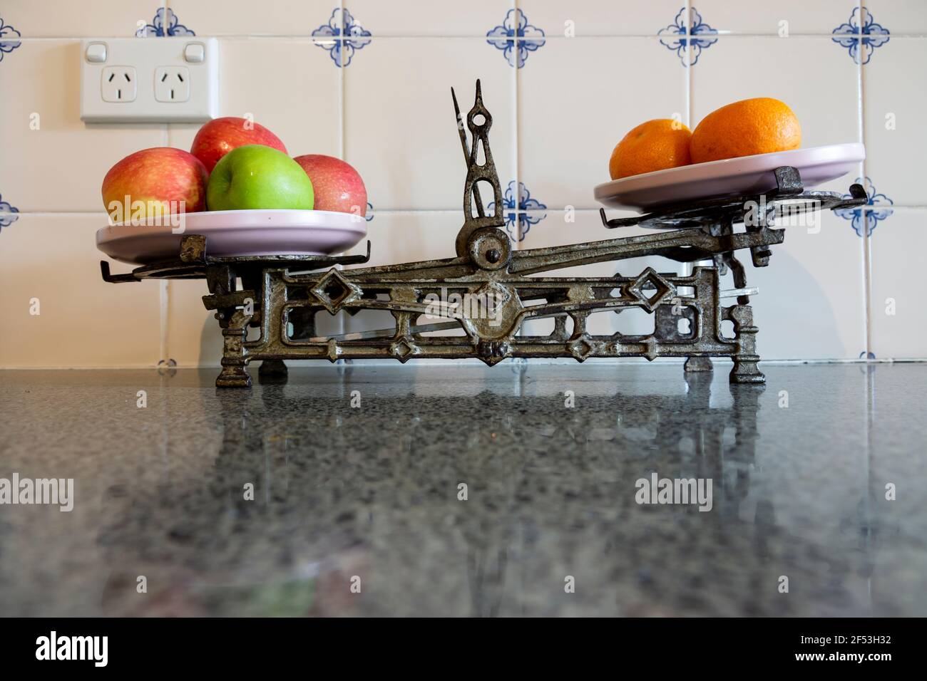 Cocina antigua retro antigua balanza de hierro cocina con manzanas rojas y verdes y naranjas en un banco de cocina de granito. Foto de stock