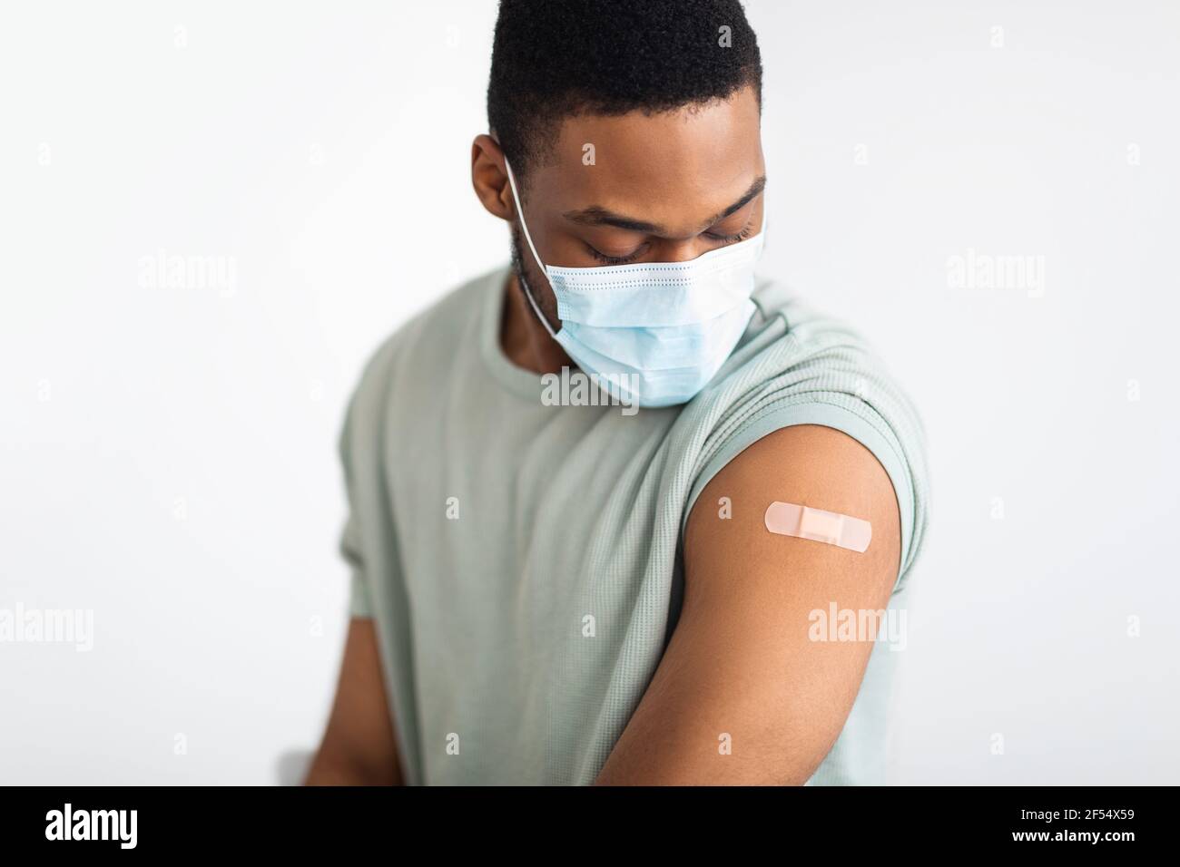 Hombre vacunado mirando el brazo con el yeso de inyección, fondo blanco Foto de stock