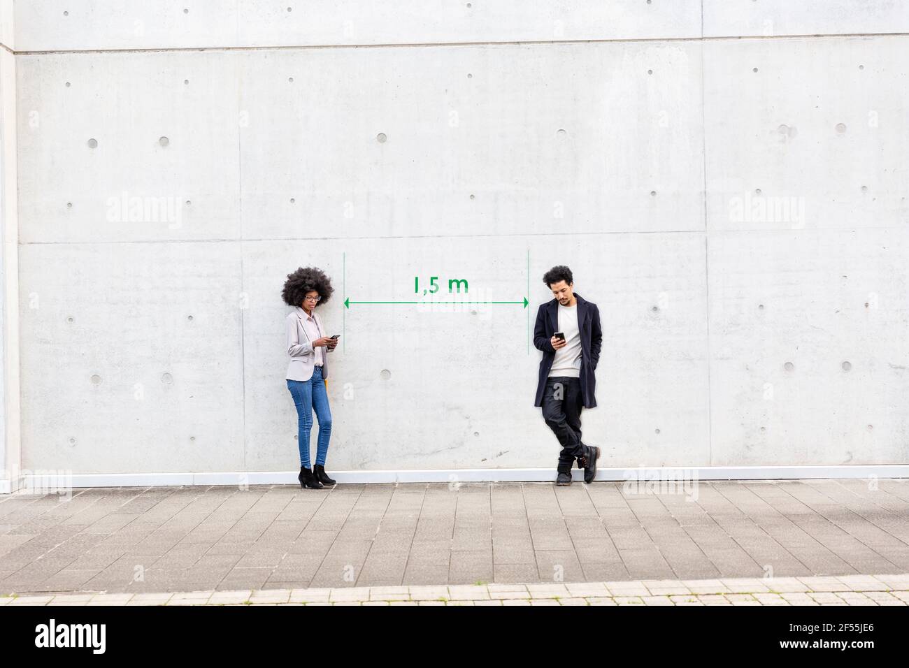 Una línea que visualiza el distanciamiento social separando al hombre y a la mujer de pie al aire libre con teléfonos inteligentes en las manos Foto de stock
