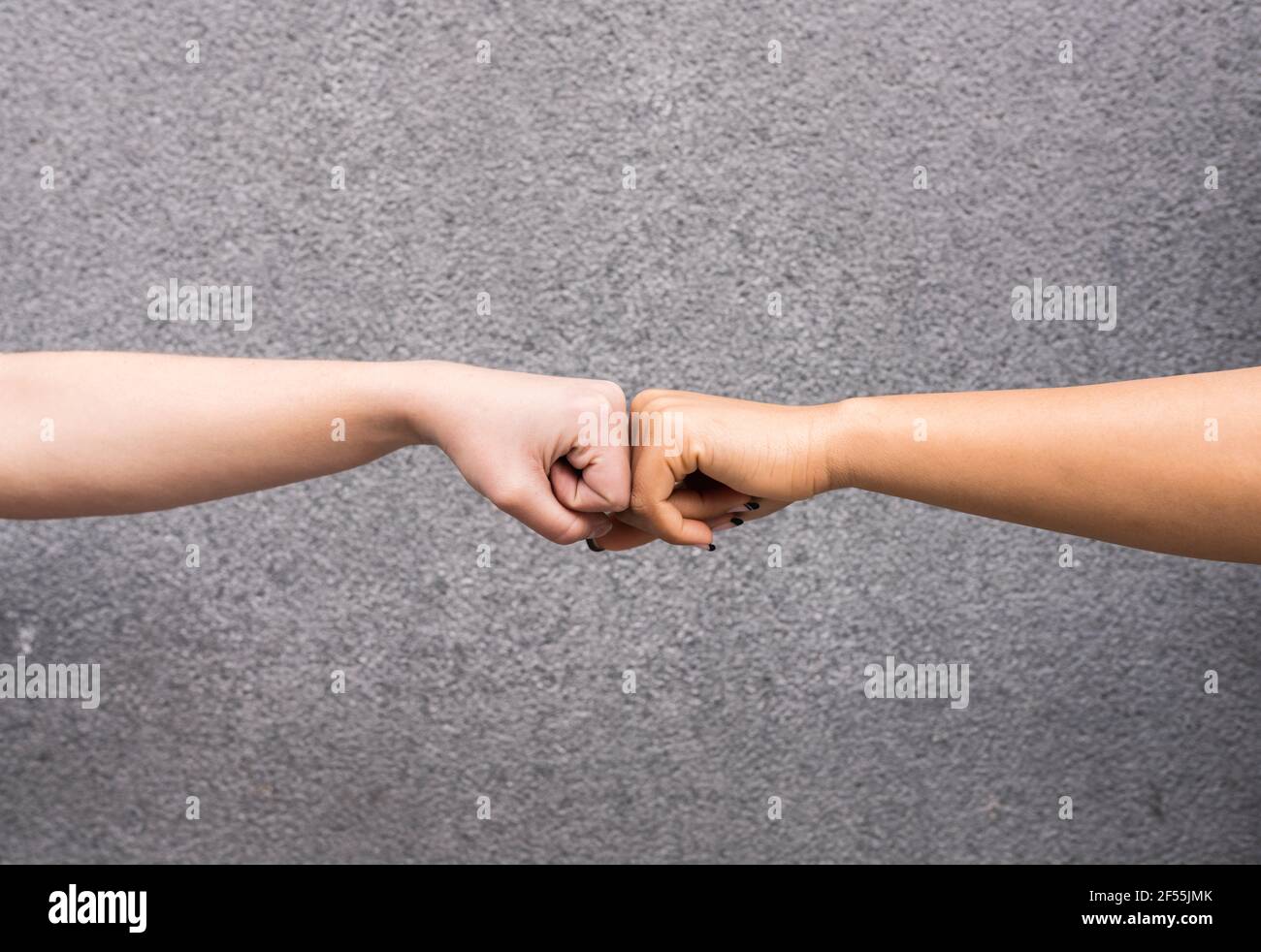 Brazos de dos mujeres jóvenes golpeando el puño sobre fondo gris Foto de stock