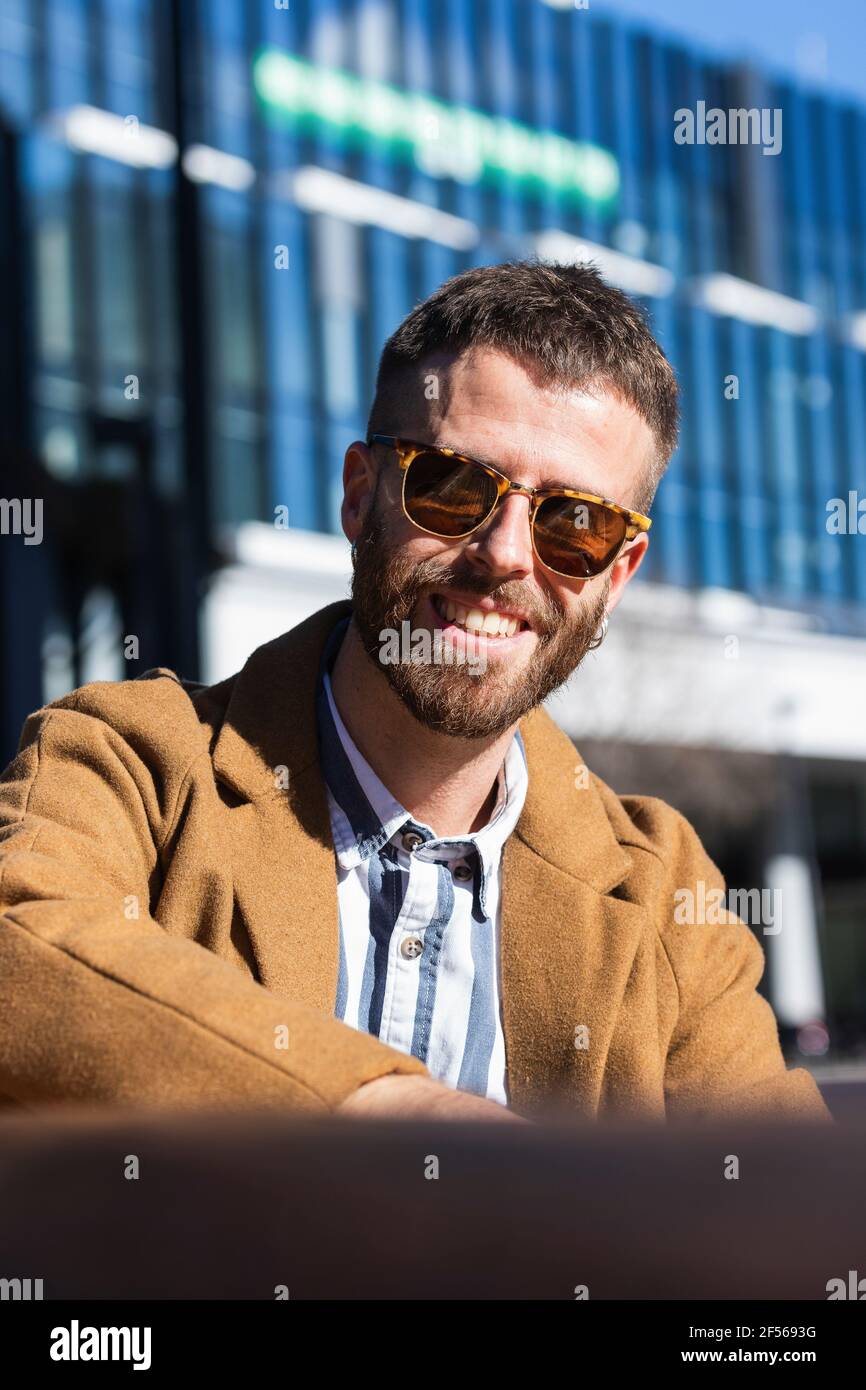 Hombre de negocios adulto medio sonriendo mientras se sienta al aire libre durante el día soleado Foto de stock