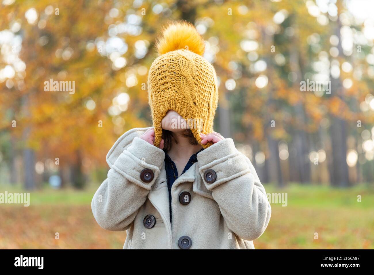 Niña tirando de gorro de punto mientras juega en el bosque Foto de stock