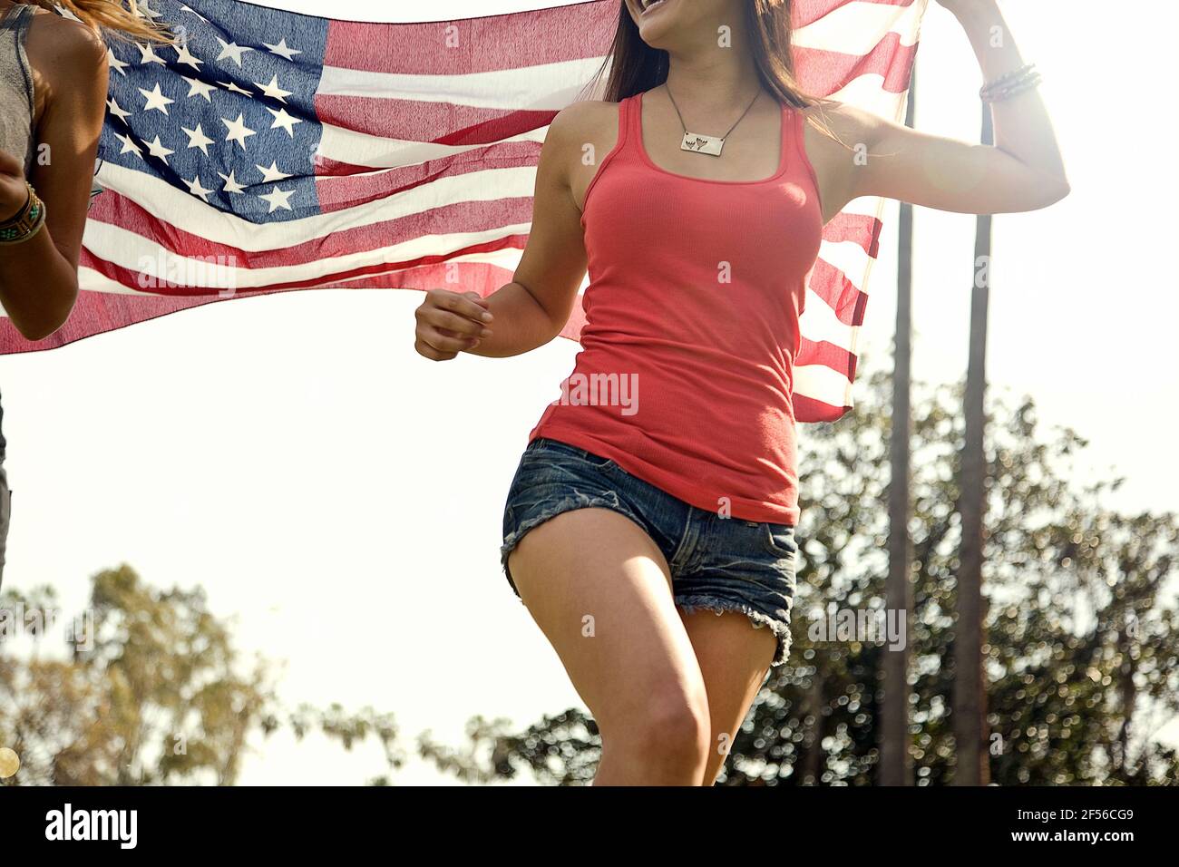 Mujeres que tienen bandera americana mientras corren en el parque durante el sol día Foto de stock