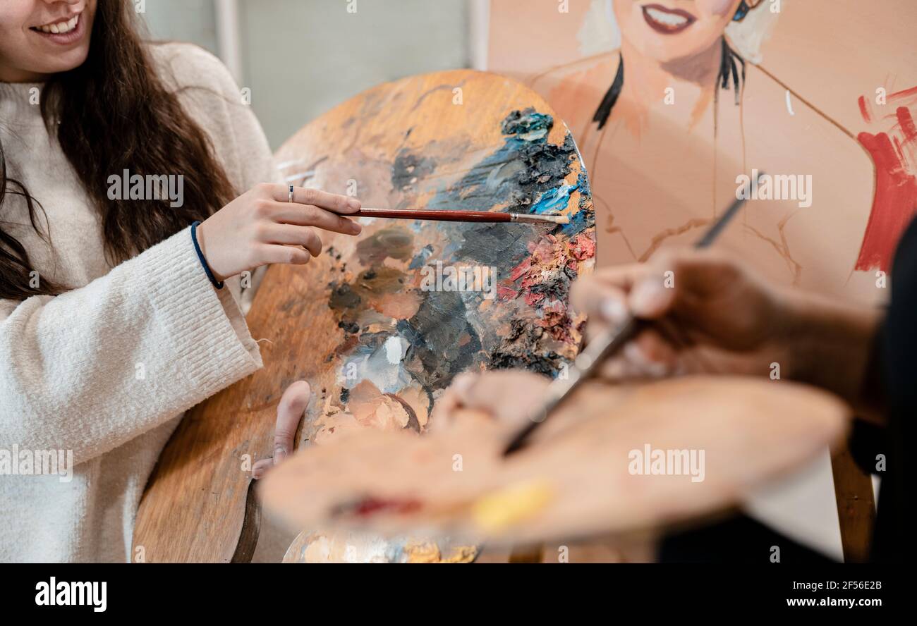 Jóvenes artistas femeninas sosteniendo paletas mientras pintan en el estudio de arte Foto de stock
