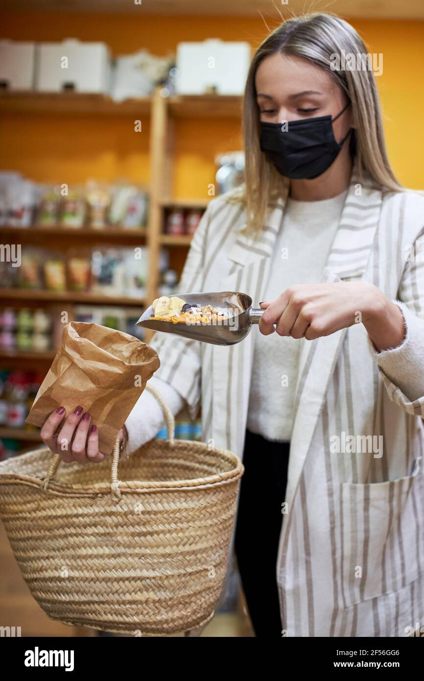 Mujer con mascarilla protectora vertiendo alimentos orgánicos en papel bolsa en la tienda Foto de stock