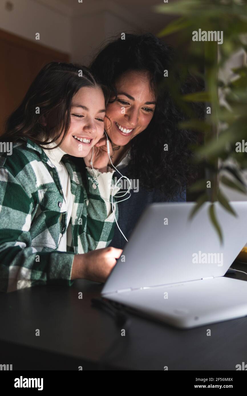 Chica sonriente con auriculares e-learning a través del portátil de la madre en inicio Foto de stock