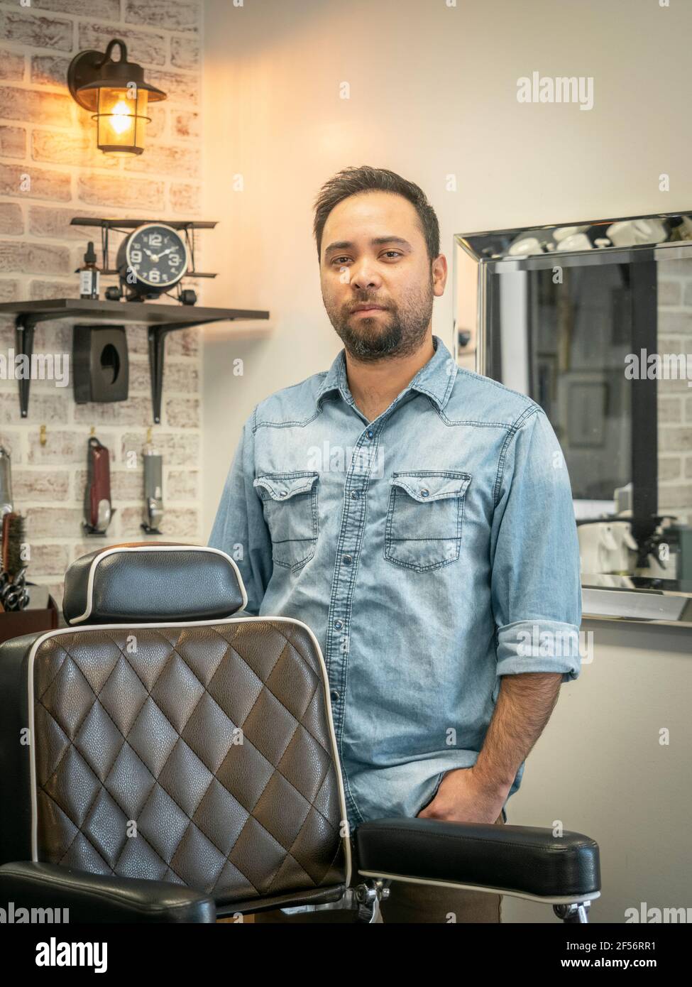 Hispano o latino, latino, barber masculino de pie frente a su silla de barber en su tienda de barber propiedad minoritaria en Pike Road Alabama, Estados Unidos. Foto de stock