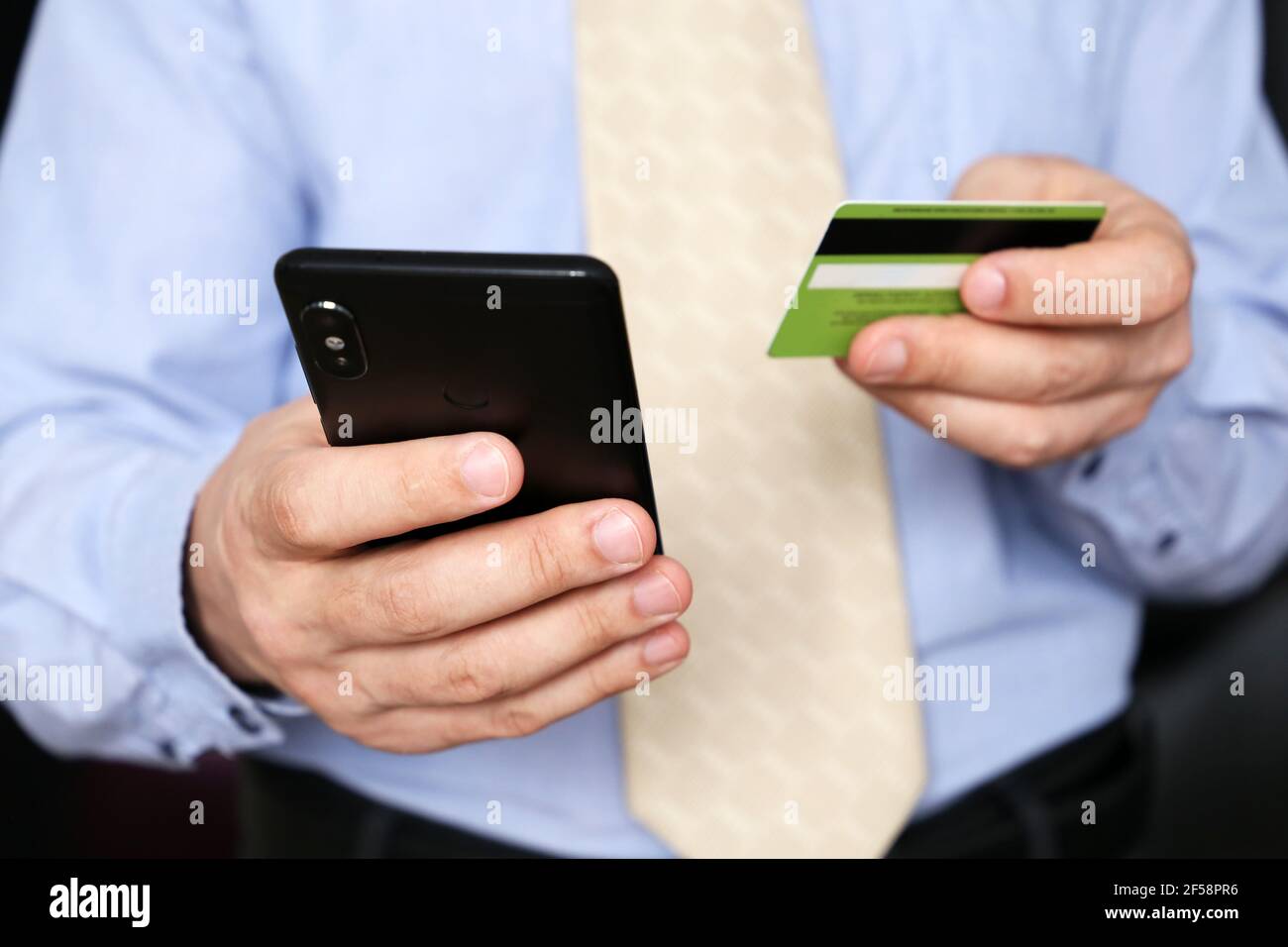Hombre en ropa de oficina con tarjeta bancaria de crédito y smartphone en las manos. Concepto de compra y pago en línea, transacción financiera Foto de stock