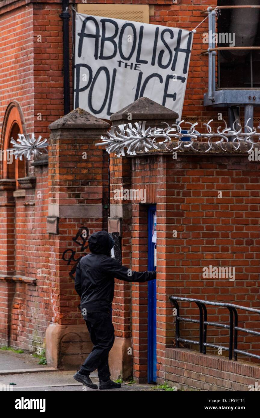 Londres, Reino Unido. 25 de marzo de 2021. Los ocupantes ilegales vuelven a entrar a través de una puerta lateral - bajo una bandera de la policía abolida - los ocupantes ilegales y activistas han ocupado la antigua comisaría de policía común de Clapham para exigir "la retirada de la policía, el crimen, Sentencia y tribunales Bill y el fin del femicidio recientemente destacado por el asesinato de Sarah Everard por un agente de policía se reunió". Habría sido la estación más cercana a donde Sarah fue vista por última vez. Aunque el proyecto de ley se ha pospuesto actualmente, quieren asegurarse de que no se apruebe y también están tratando de destacar la Sección 4 del proyecto de ley, que criminal Foto de stock