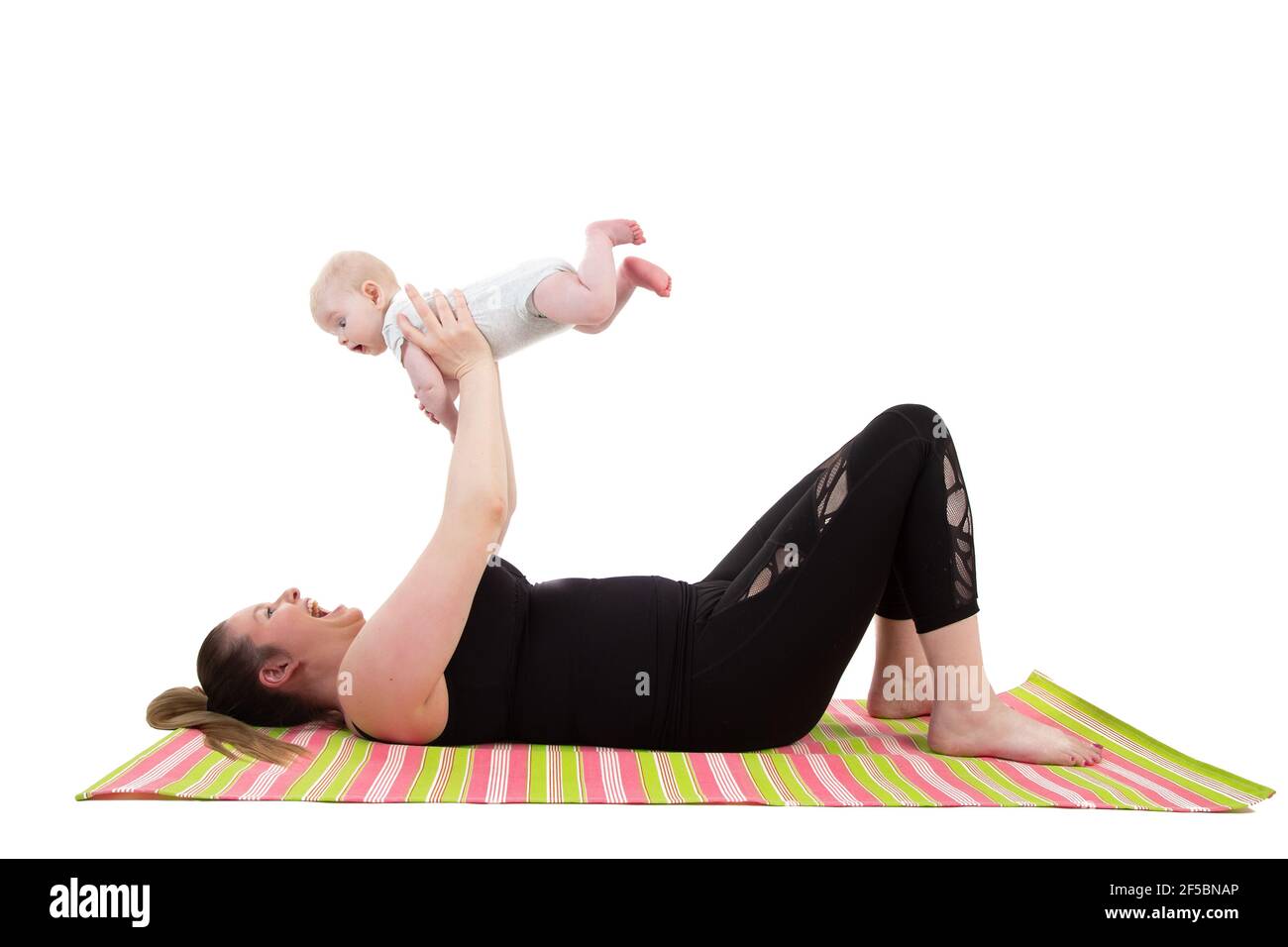 madre con bebé divertirse sosteniendo al bebé en el aire mientras se pone en una alfombra de fitness Foto de stock