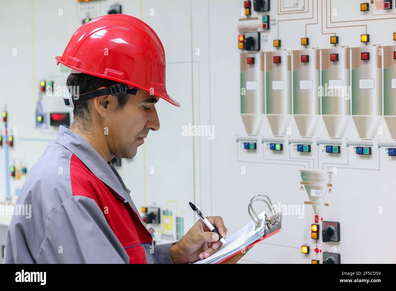 Ingeniero de pie frente al panel de control de la sala de instrumentación y escribe los resultados de las mediciones. Foto de stock