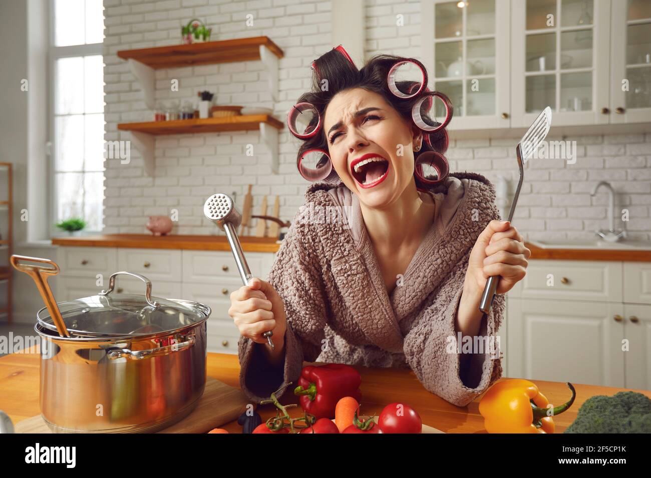 Joven ama de casa infeliz enferma y cansada de cocinar y hacer las tareas domésticas llorando en la cocina Foto de stock