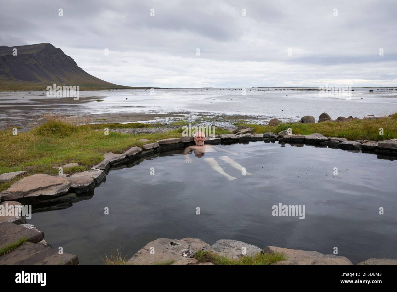 Hombre bañándose en la piscina geotérmica natural de Krosslaug directamente en la costa, Islandia, Birkimelur Foto de stock