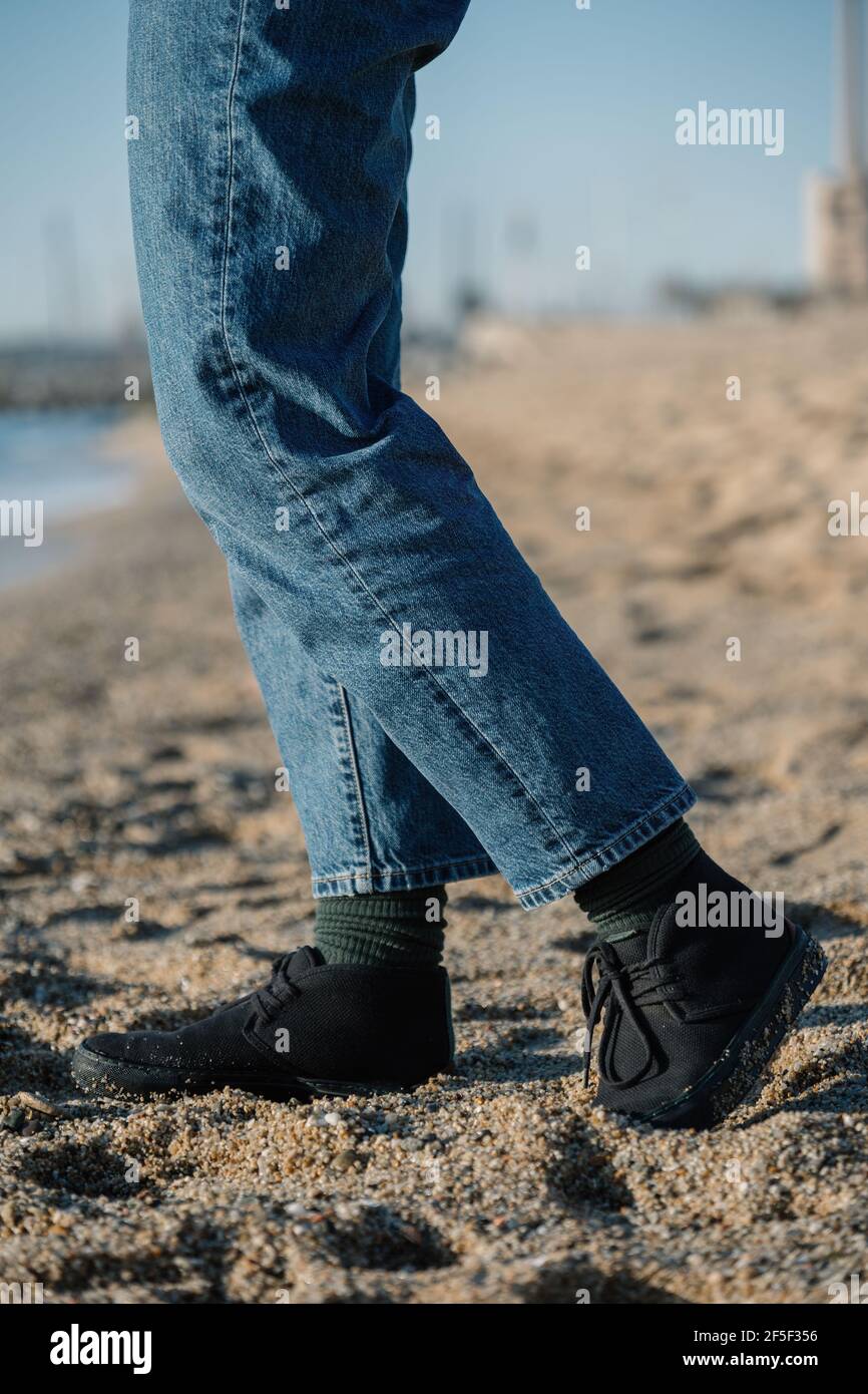 Gallina Dolor absceso Piernas de hombre en jeans y calcetines verdes en la arena en una playa.  Caminar en zapatos cómodos en la playa Fotografía de stock - Alamy