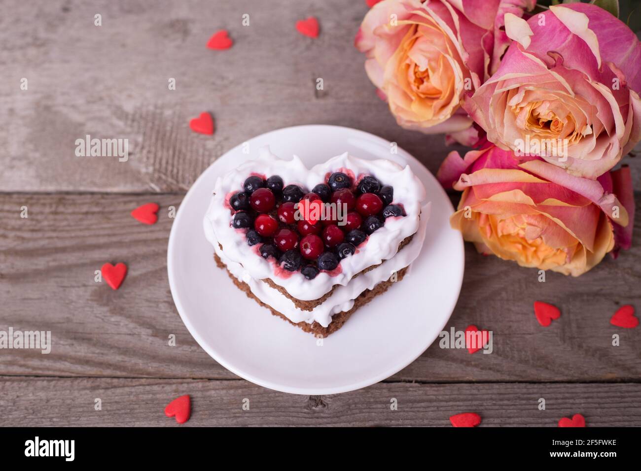 Mini pastel de postre romántico para el día de San Valentín con rosas.  Galletas dulces con relleno de crema y corazón rojo para la decoración  sobre fondo de madera. Primer plano, CO