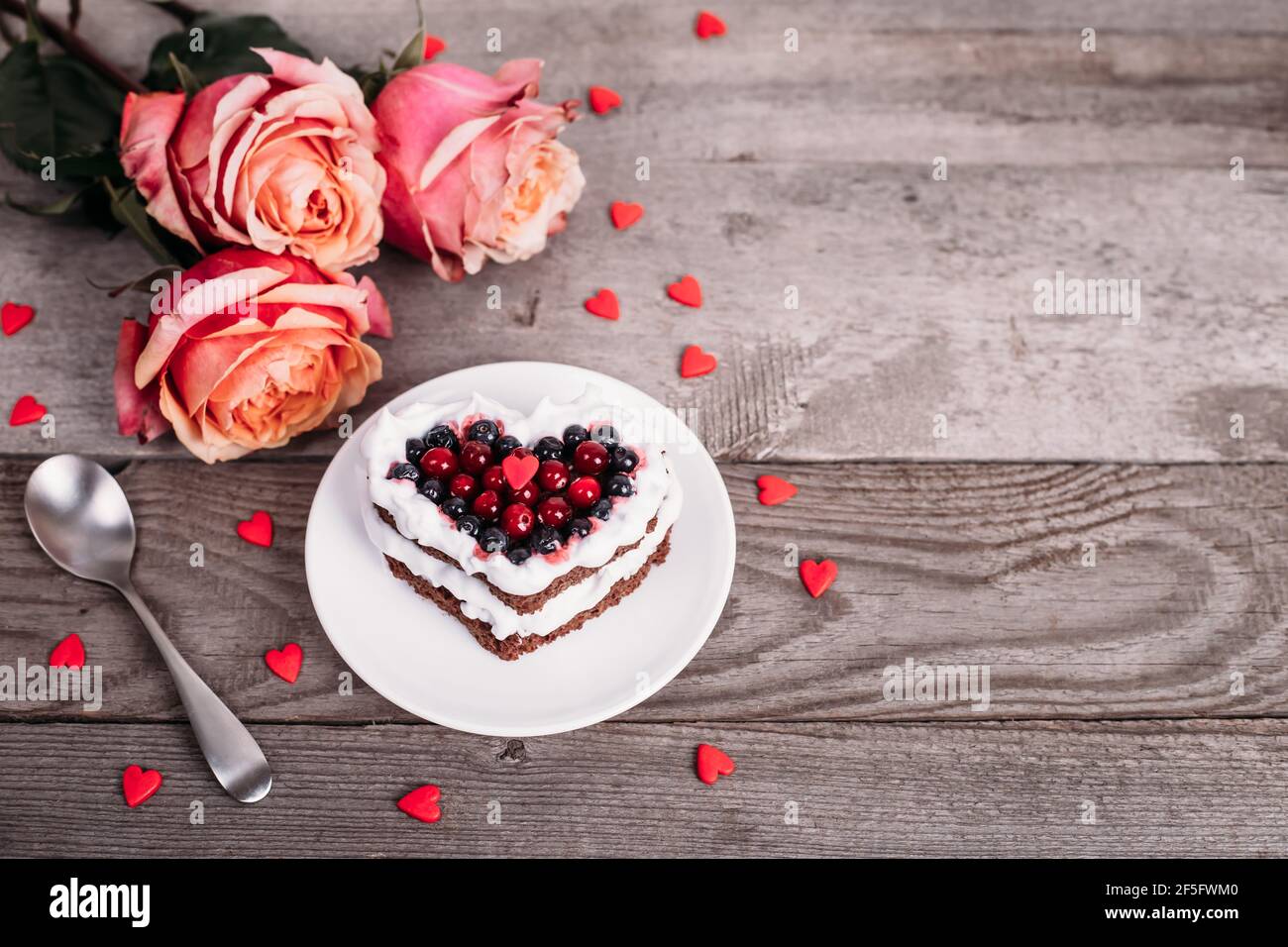 Mini pastel de postre romántico para el día de San Valentín con rosas.  Galletas dulces con relleno de crema y corazón rojo para la decoración  sobre fondo de madera. Primer plano, CO