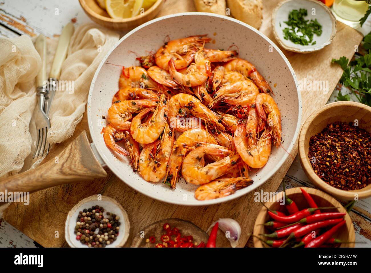 Langostinos asados en sartén servidos en tabla de corte de madera blanca Foto de stock