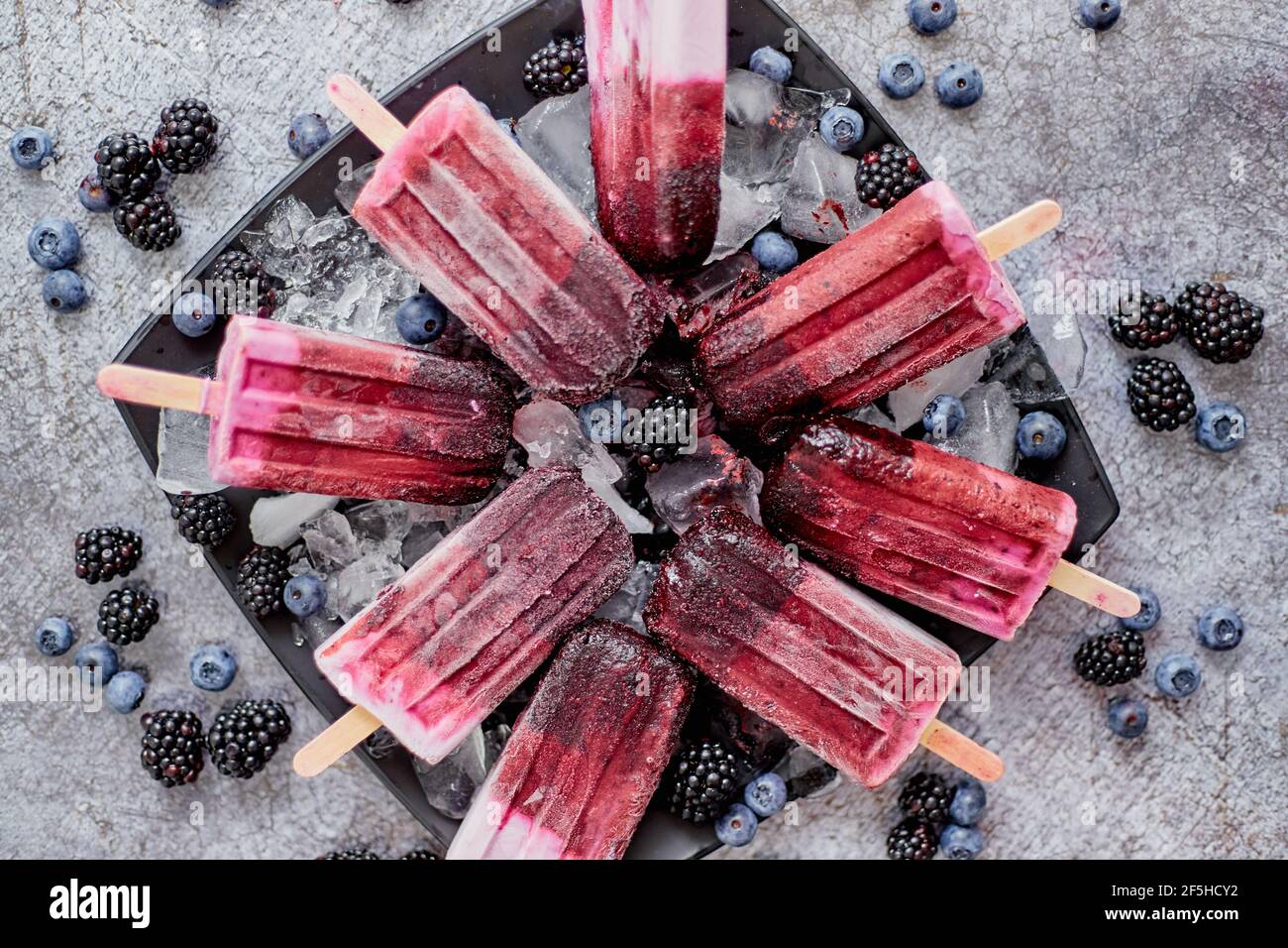 Helados caseros de arándanos frescos y paletas de blackberry en un plato negro con hielo sentado en piedra Foto de stock