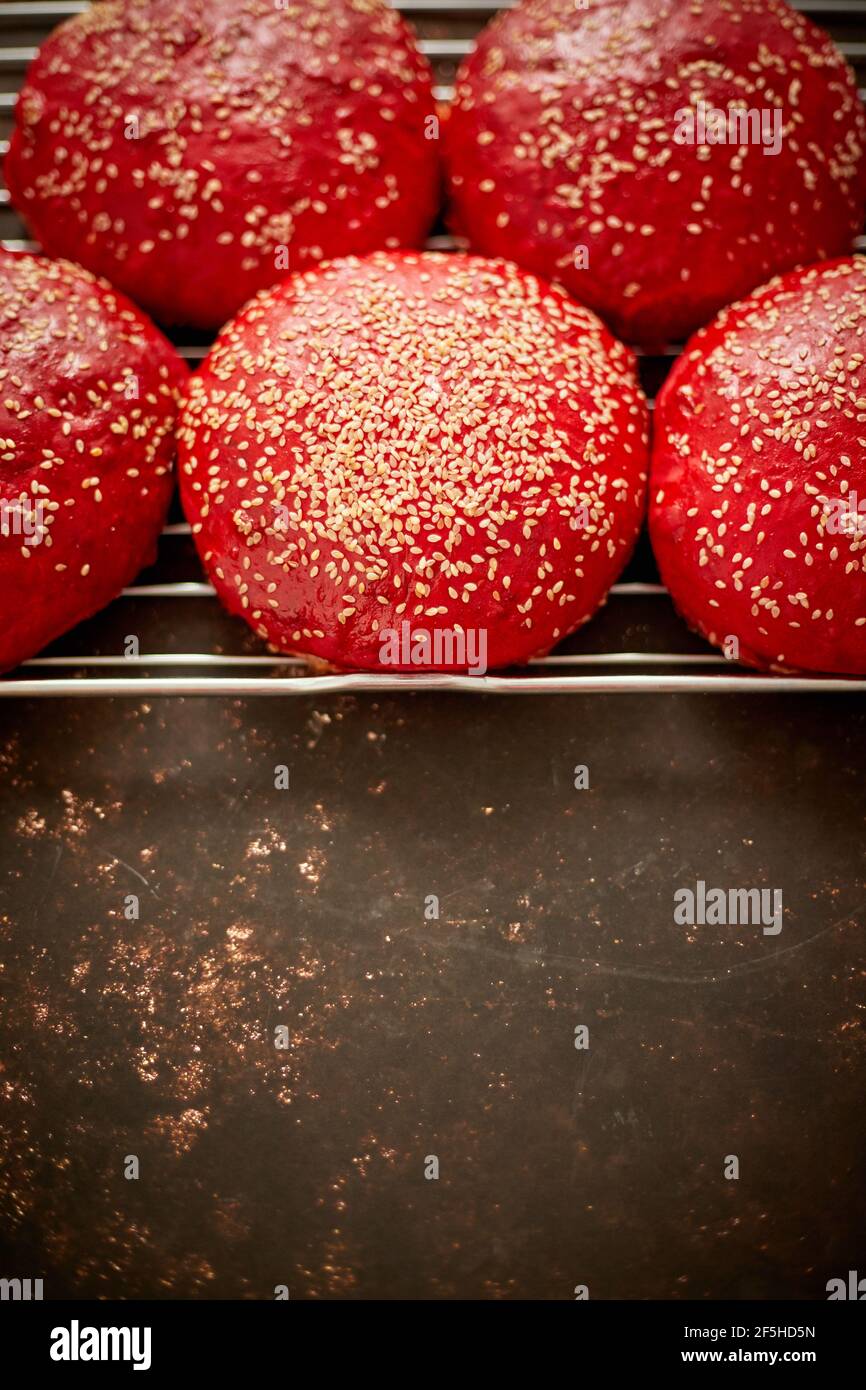 Panecillos de hamburguesa caseros de color rojo recién horneados con vista superior de sésamo. Se coloca en una parrilla de metal. Foto de stock