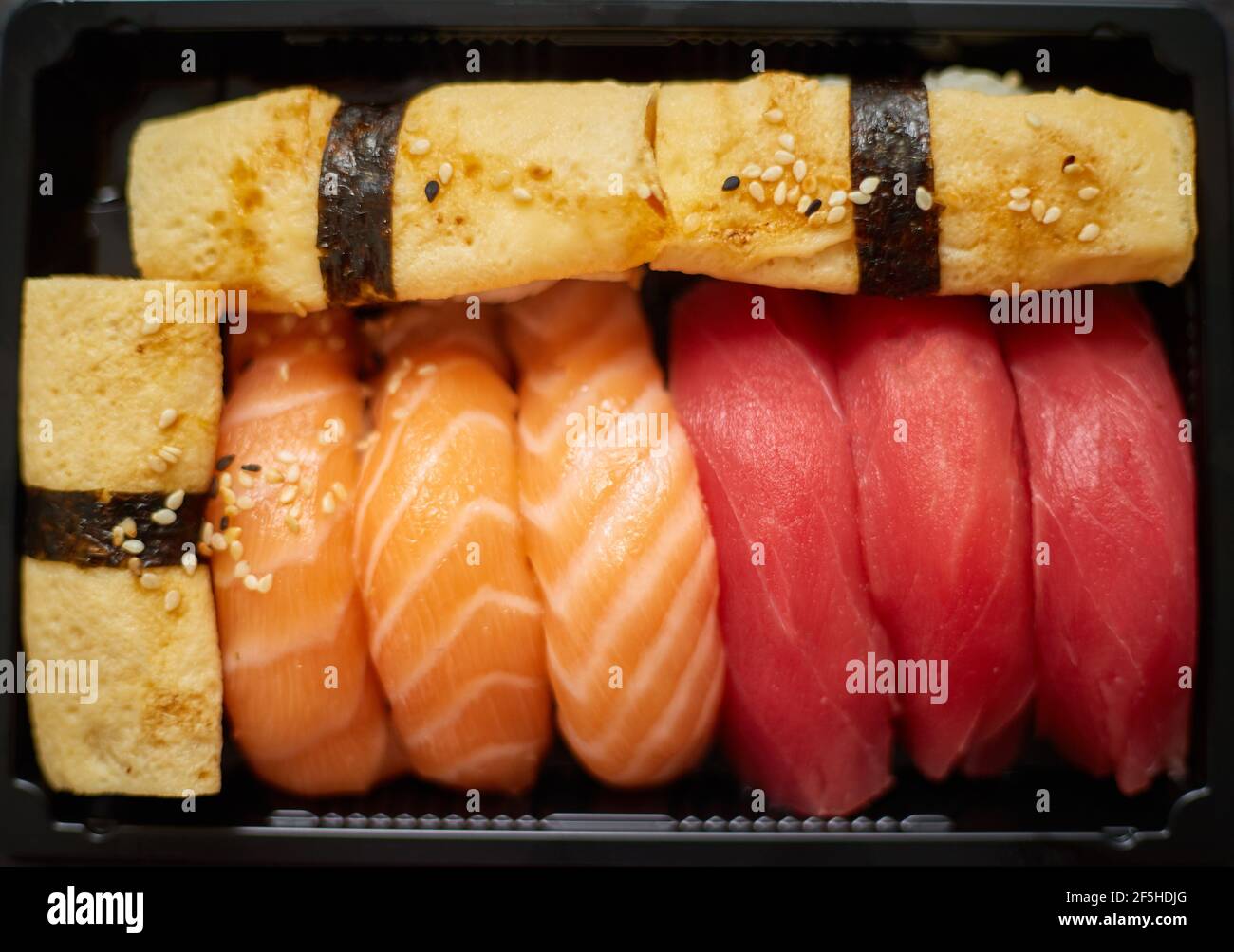 El sushi nigiri se prepara en un recipiente de plástico listo para la entrega para llevar. Cierre de la caja de comida para llevar Foto de stock