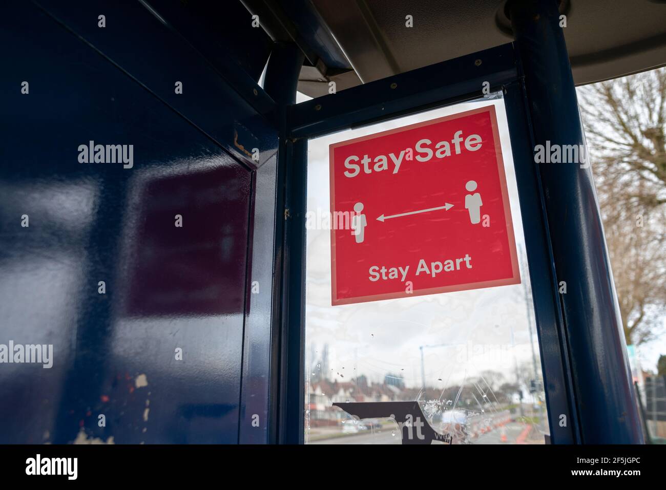 Stay Safe Stay Apart señal roja de distanciamiento social con dos caracteres blancos separados por una flecha de dos lados, en una ventana de parada de autobús en el Reino Unido Foto de stock