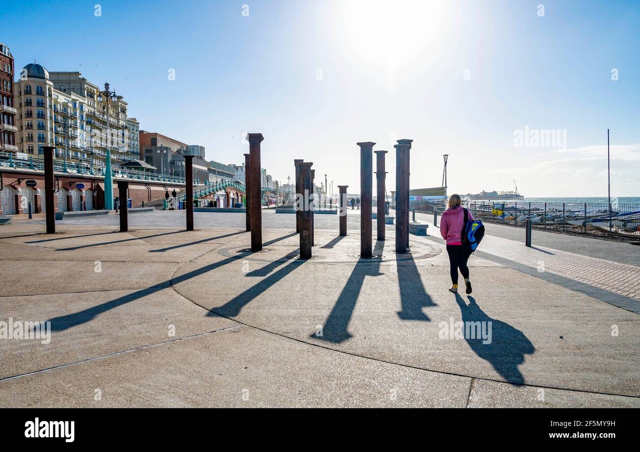 Brighton Reino Unido 27th Marzo 2021 - Caminantes Disfrute de una mañana soleada pero fría por la instalación de arte Golden Spiral en el paseo marítimo de Brighton. Se prevé que el clima se vuelva mucho más cálido la próxima semana, con temperaturas que se espera alcancen más de 20 grados en algunas partes del Reino Unido: Crédito Simon Dack / Alamy Live News Foto de stock