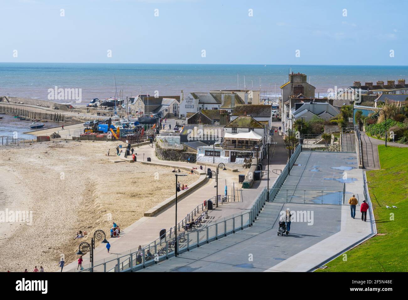 Lyme Regis, Dorset, Reino Unido. 27th de marzo de 2021. Tiempo en el Reino Unido: Después de un comienzo frío, había un montón de rachas de sol en la estación costera de Lyme Regis hoy. La gente de la zona estaba a punto de disfrutar del sol de primavera, pero la playa era tranquila para esta época del año. Se espera que la bonita ciudad costera esté más ocupada la próxima semana, ya que las restricciones de bloqueo de coronavirus finalmente comienzan a aliviarse. Crédito: Celia McMahon/Alamy Live News Foto de stock