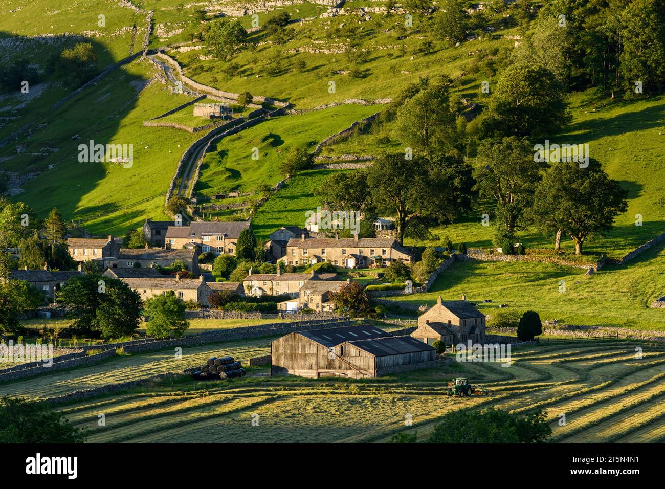Pintoresco valle de Dales y pequeño pueblo, casas, granero, campos de cultivo, colina, Empinada ladera y tractor de heno - Starbotton, Yorkshire, Inglaterra Reino Unido. Foto de stock