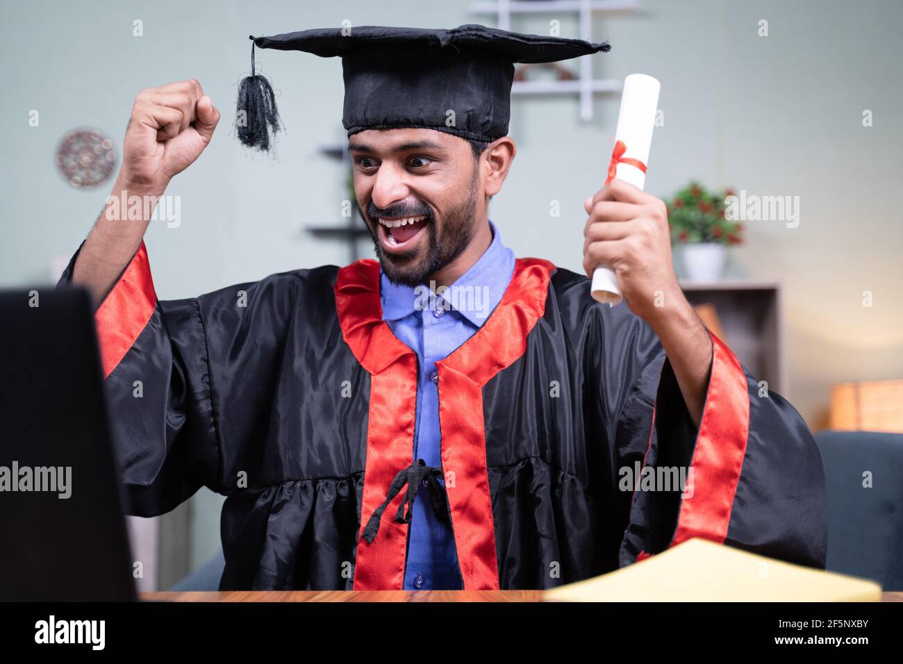Un hombre joven se emocionó por anunciar los nombres de graduación a través de la videollamada mientras que la celebración de certificado - concepto de graduación virtual nuevo normal debido a covid-19 Foto de stock