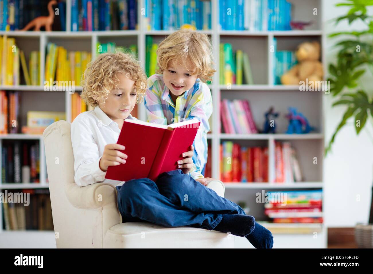 Libro de lectura para niños. Los niños leen. Niño pequeño en una estantería  llena de color haciendo la tarea para la escuela. Estudiante con libros.  Educación temprana y desarrollo Fotografía de stock -
