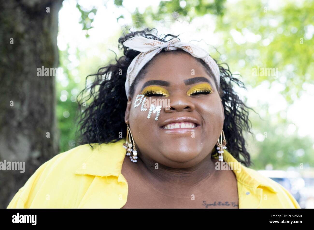 Hermosa, feliz Chica Afro-Americana sonriente con BLM en la mejilla y usando amarillo Foto de stock