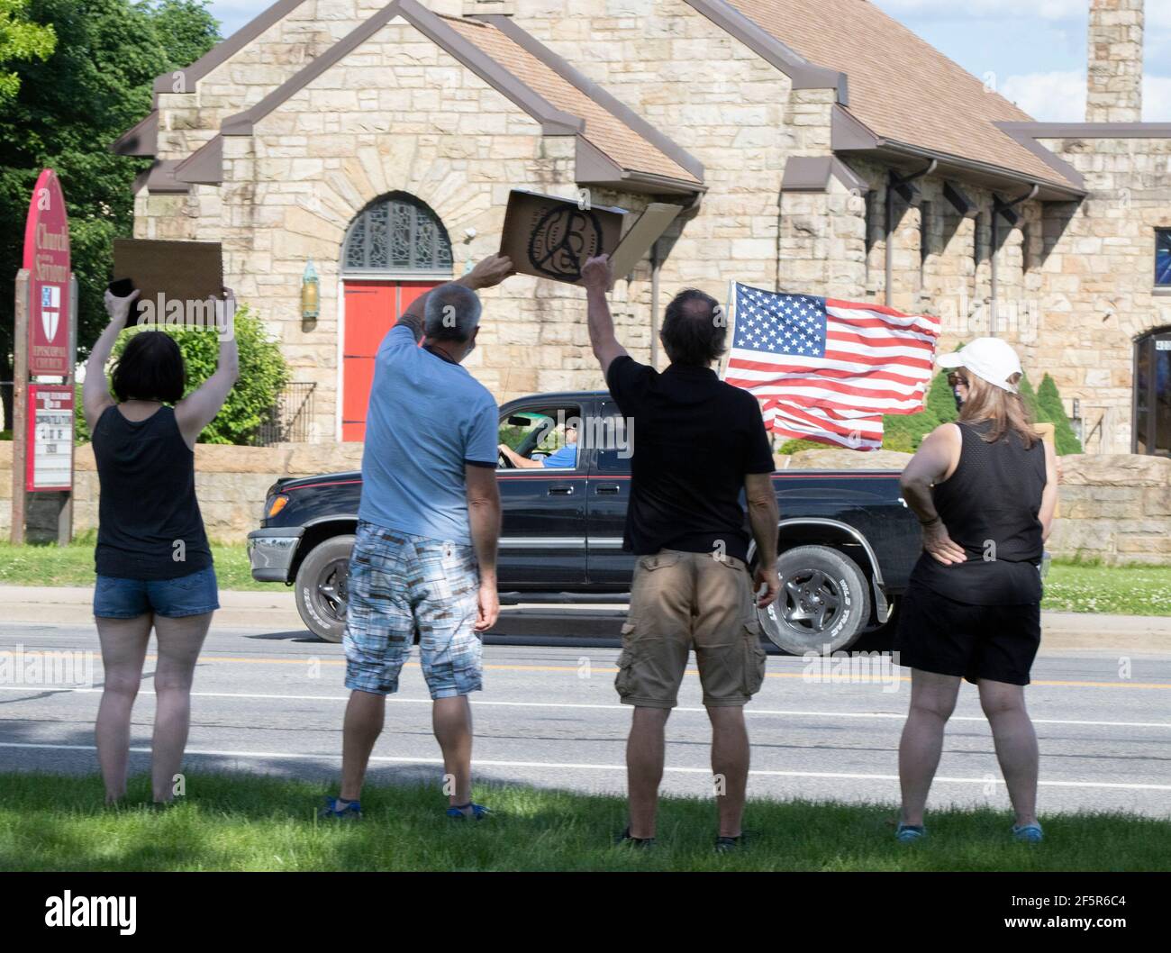 Hombres blancos y mujeres sosteniendo el signo de paz durante la paz Protesta con el camión y la bandera americana conduciendo Foto de stock