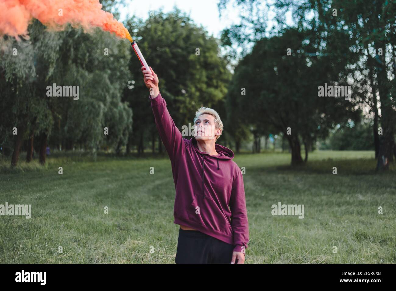 Hombre estilo calle en hoodie sostener la mano llamarada con la bomba de granada de humo rojo. Foto de stock