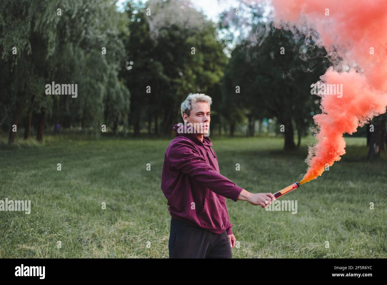 Hombre estilo calle en hoodie sostener la mano llamarada con la bomba de granada de humo rojo. Foto de stock