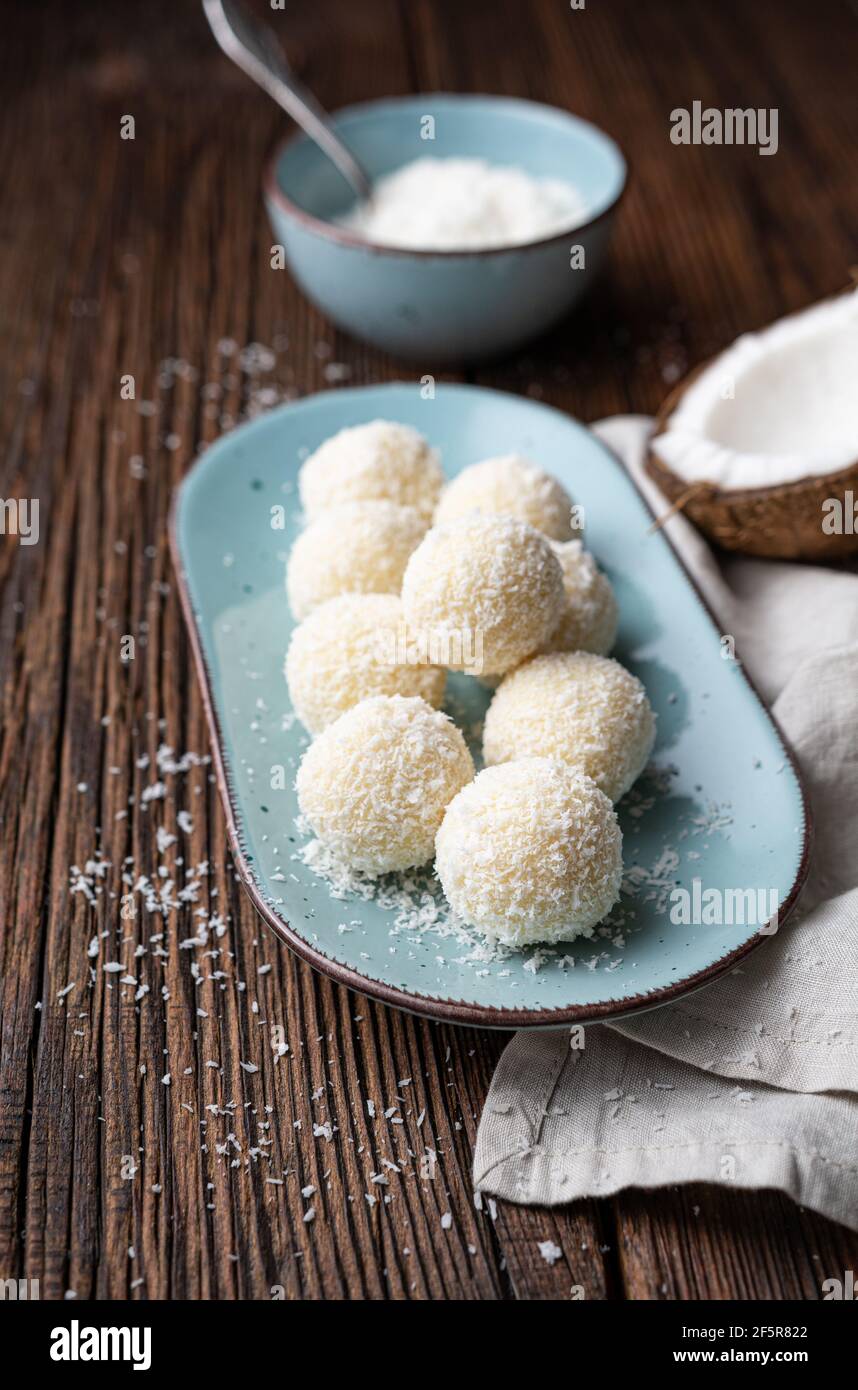 Delicioso caramelo sin hornear, trufas de chocolate blanco cubierto de coco rallado sobre fondo de madera rústica Foto de stock