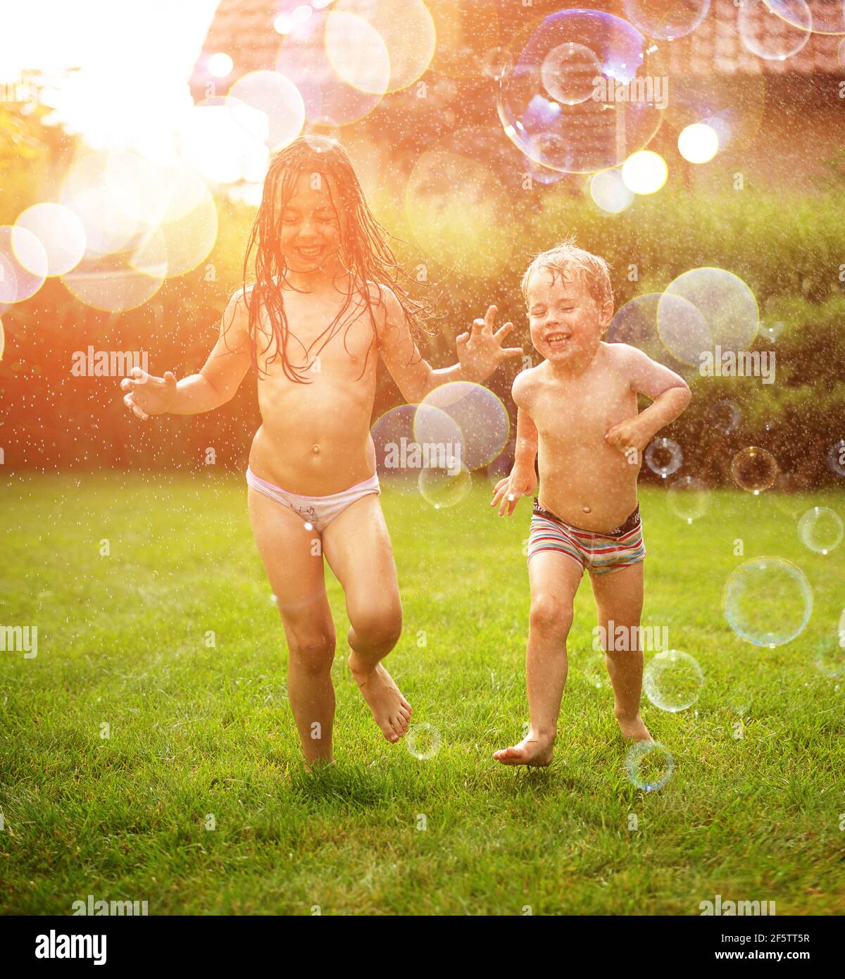 Niños alegres disfrutando de la ducha de verano en el jardín Foto de stock