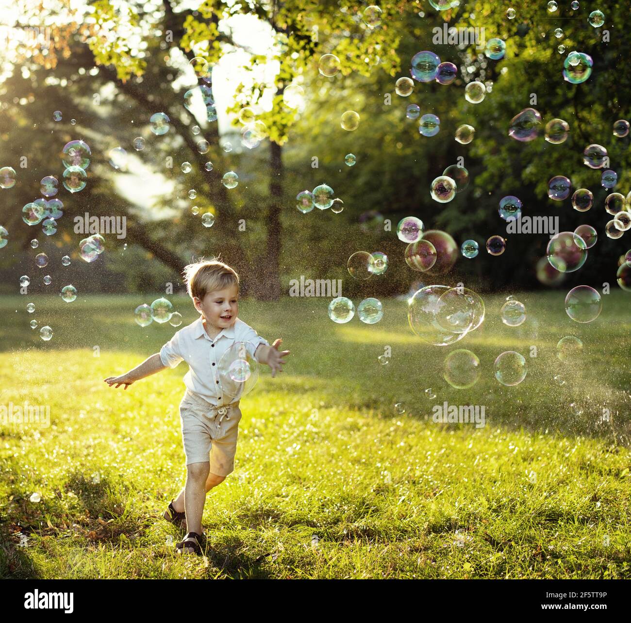 Lindo y pequeño niño persiguiendo burbujas de jabón Foto de stock