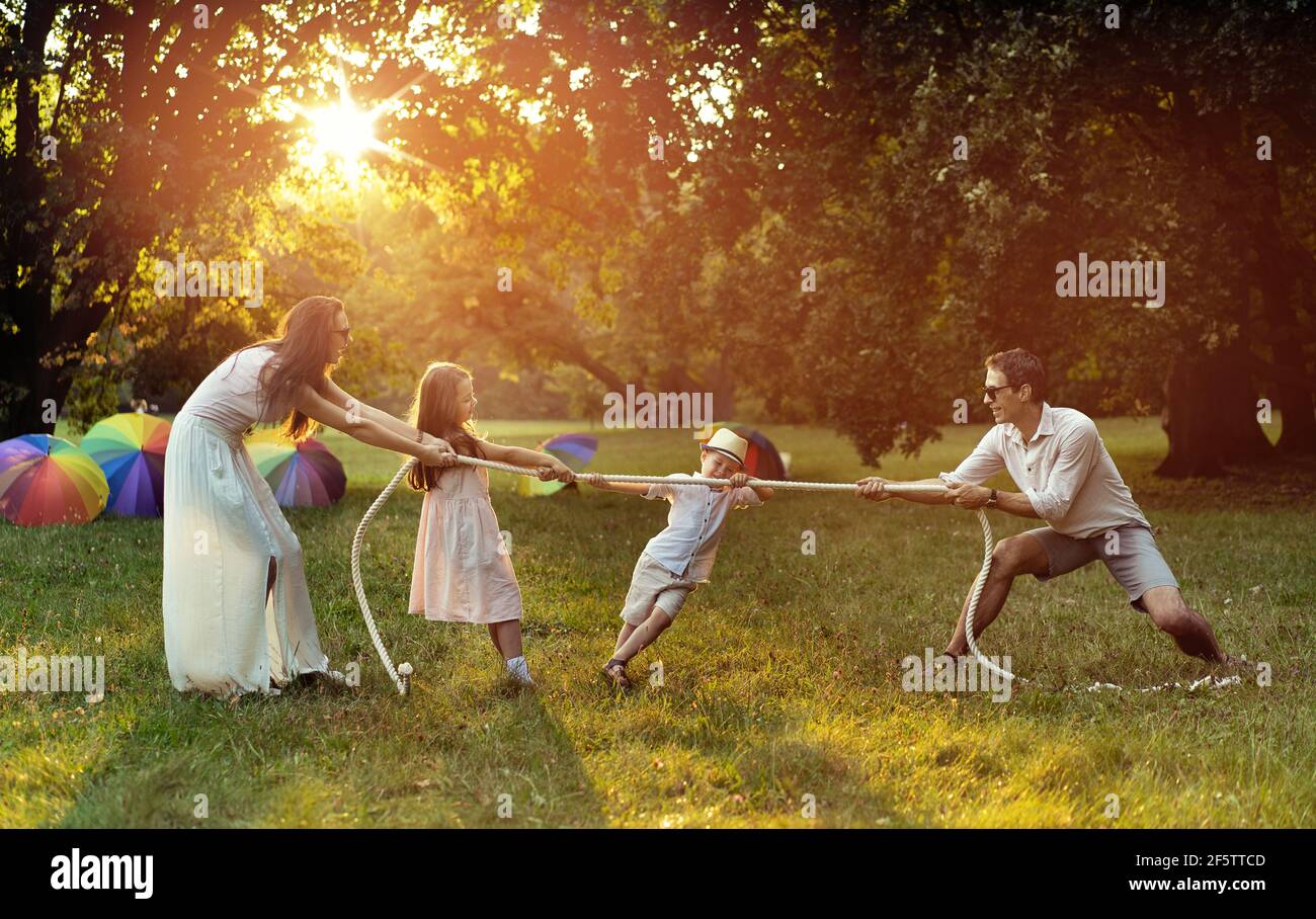 Familia joven y alegre jugando al tirón de la guerra en el parque Foto de stock