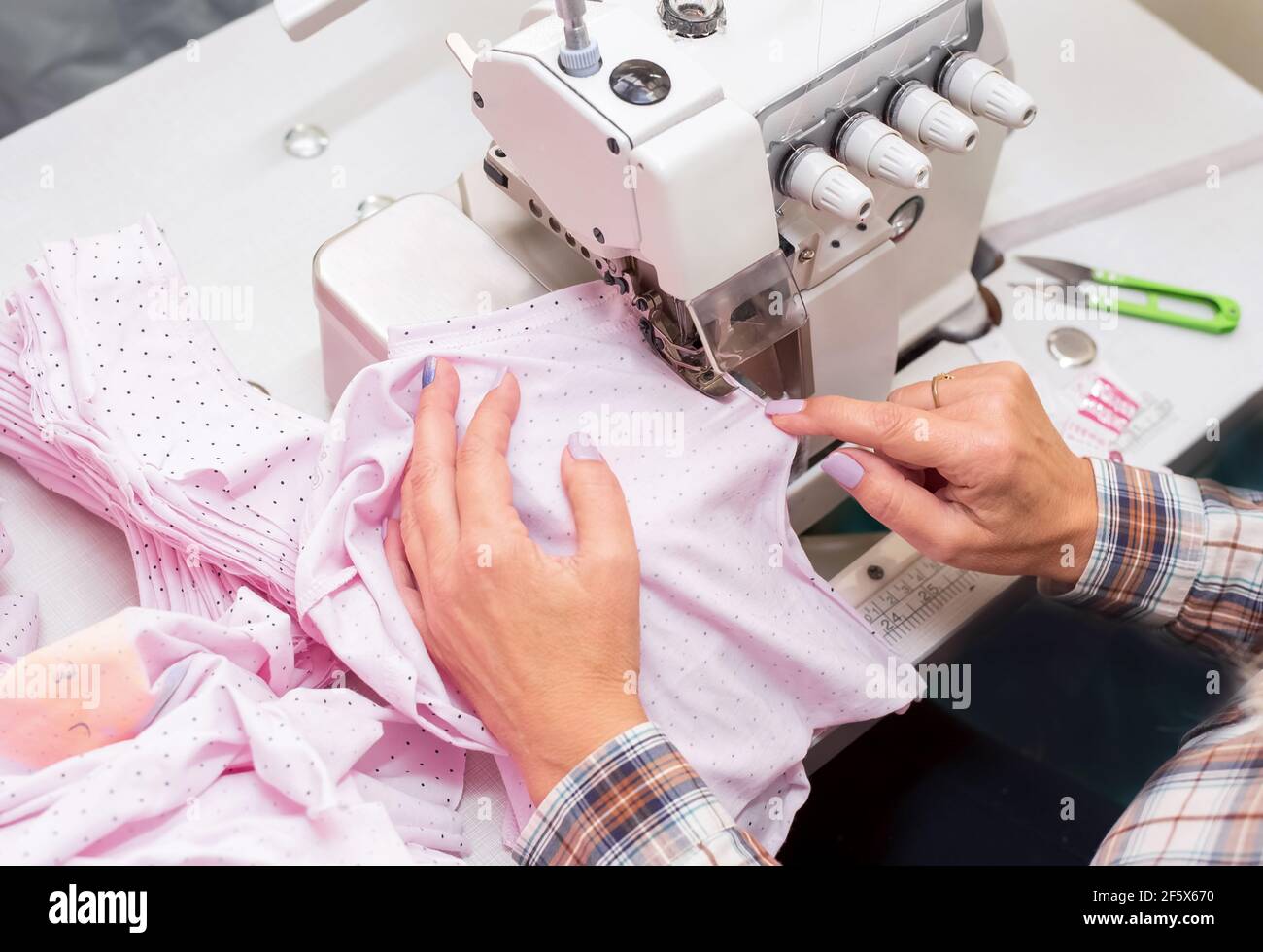 La mano femenina cosiendo ropa de bebé en la máquina overlock, fabricación de ropa. Primer plano del proceso de costura en la fábrica Fotografía de stock -