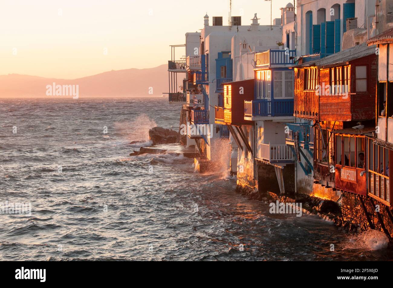 Vista panorámica del pueblo de la isla de Mykonos con terrazas y balcones con vistas al mar de las casas características de Grecia. En segundo plano Foto de stock