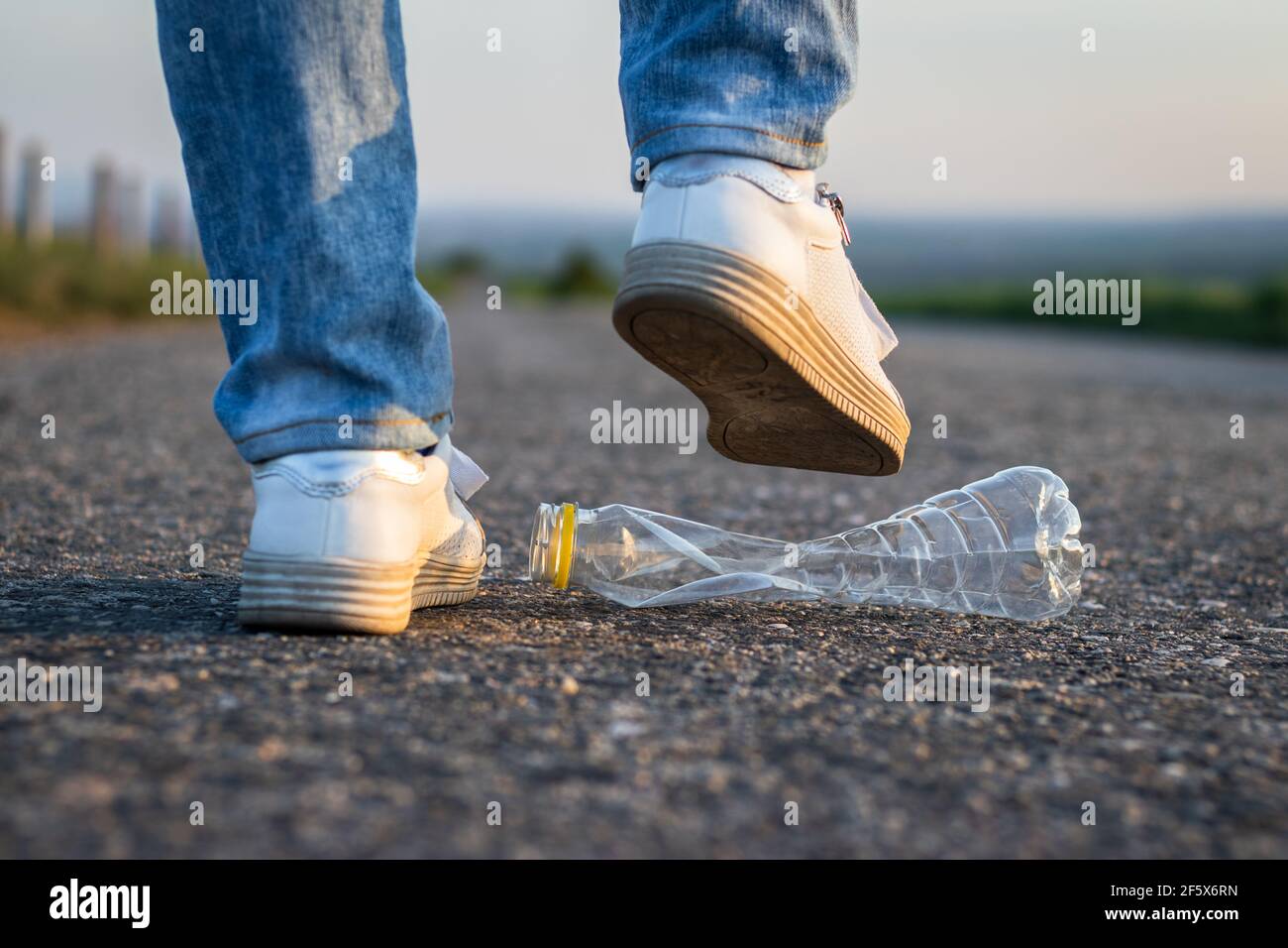 Las piernas aplastan la botella de plástico en la carretera. Conservación del medio ambiente. Residuos de plástico Foto de stock
