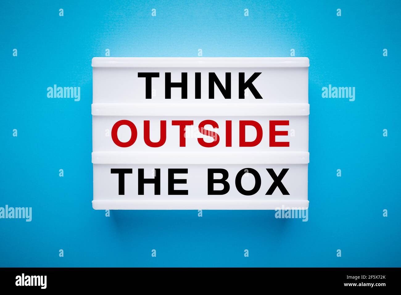 Caja de luz sobre un fondo azul claro con eslogan: Piense fuera de la caja. Foto de stock