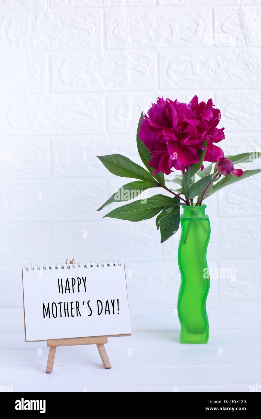 Feliz día de las madres texto escrito en el cuaderno y un peony en jarrón. Tarjeta de felicitación Foto de stock