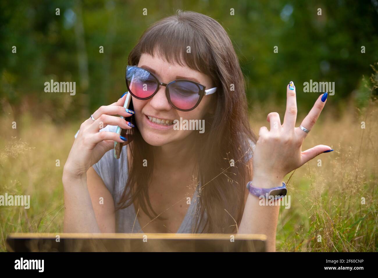 la joven habla emocionalmente por teléfono en el césped en un día soleado. feliz emoción en la cara Foto de stock